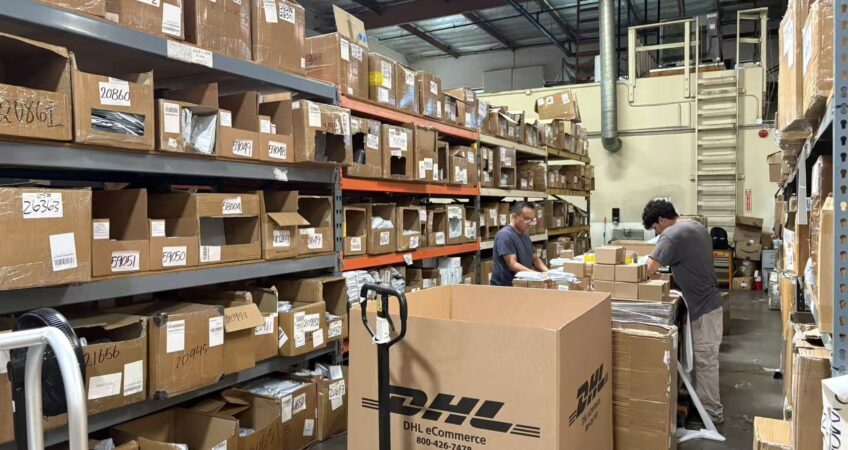 Real‑life photo of US overseas warehouse, warehouse staff sorting parcels, full storage shelves filled with cartons, DHL eCommerce large box, cross‑border seller inventory fulfillment scene