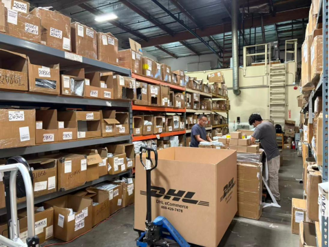 Real photo of overseas warehouse interior with workers sorting parcels and storage shelves full of cartons